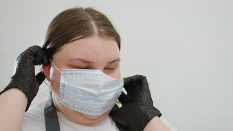 beautician with blond hair wearing black gloves adjusts protective face mask while preparing for work. focused expression highlights importance of hygiene in clean professional environment