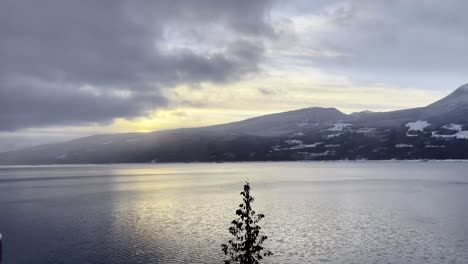 incredible reveal pan from behind a frost covered column of upper arrow lake, british columbia at halcyon hot spring resort with a beaming colorful sunset over the lake on a clear day