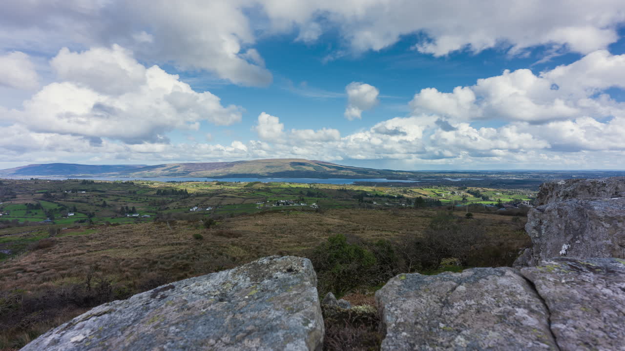 Time lapse of rural landscape with foreground of rocks and grass on hillside and lake in the distance on a spring sunny cloudy day in Arigna mountains in county Leitrim in Ireland