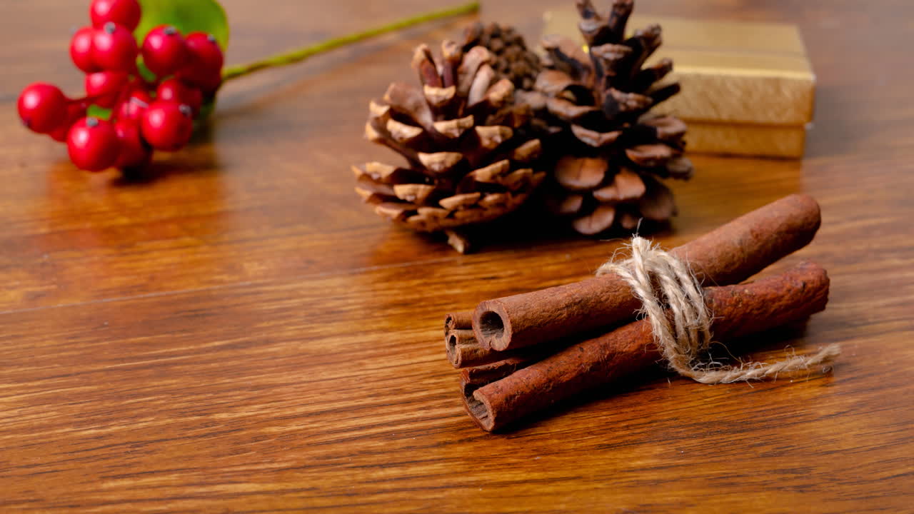 Animation of christmas decorations, cinnamon, pine cones and copy space on wooden background