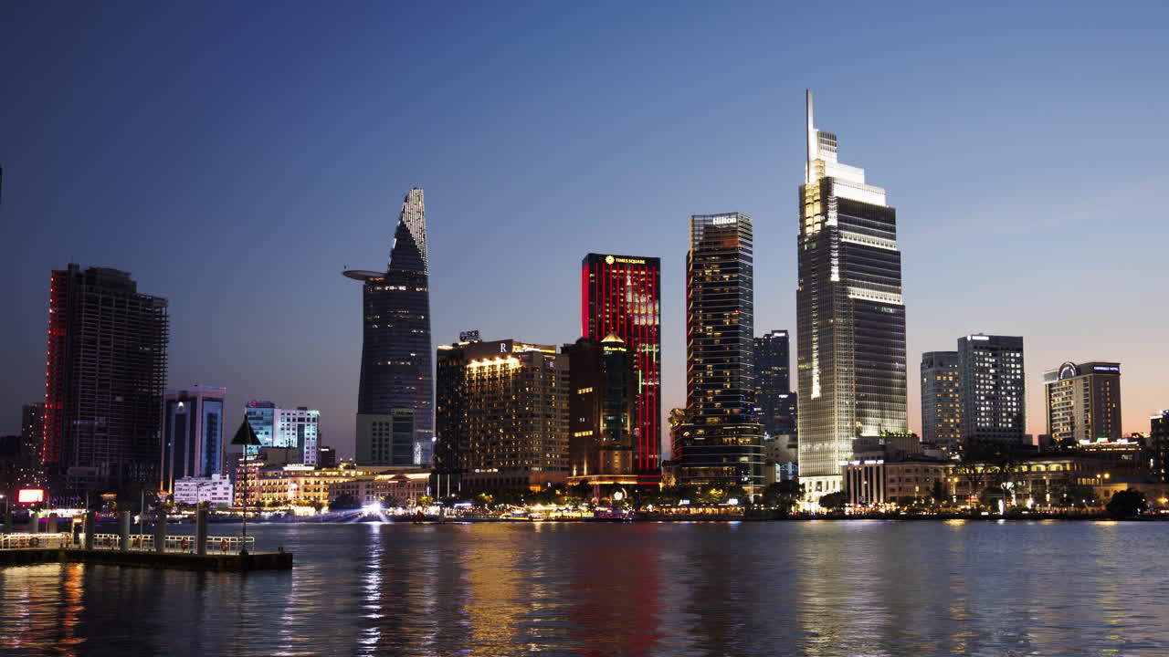 Timelapse of Saigon skyline transitioning from sunset to night, buildings lighting up and reflecting in the river as the camera zooms out