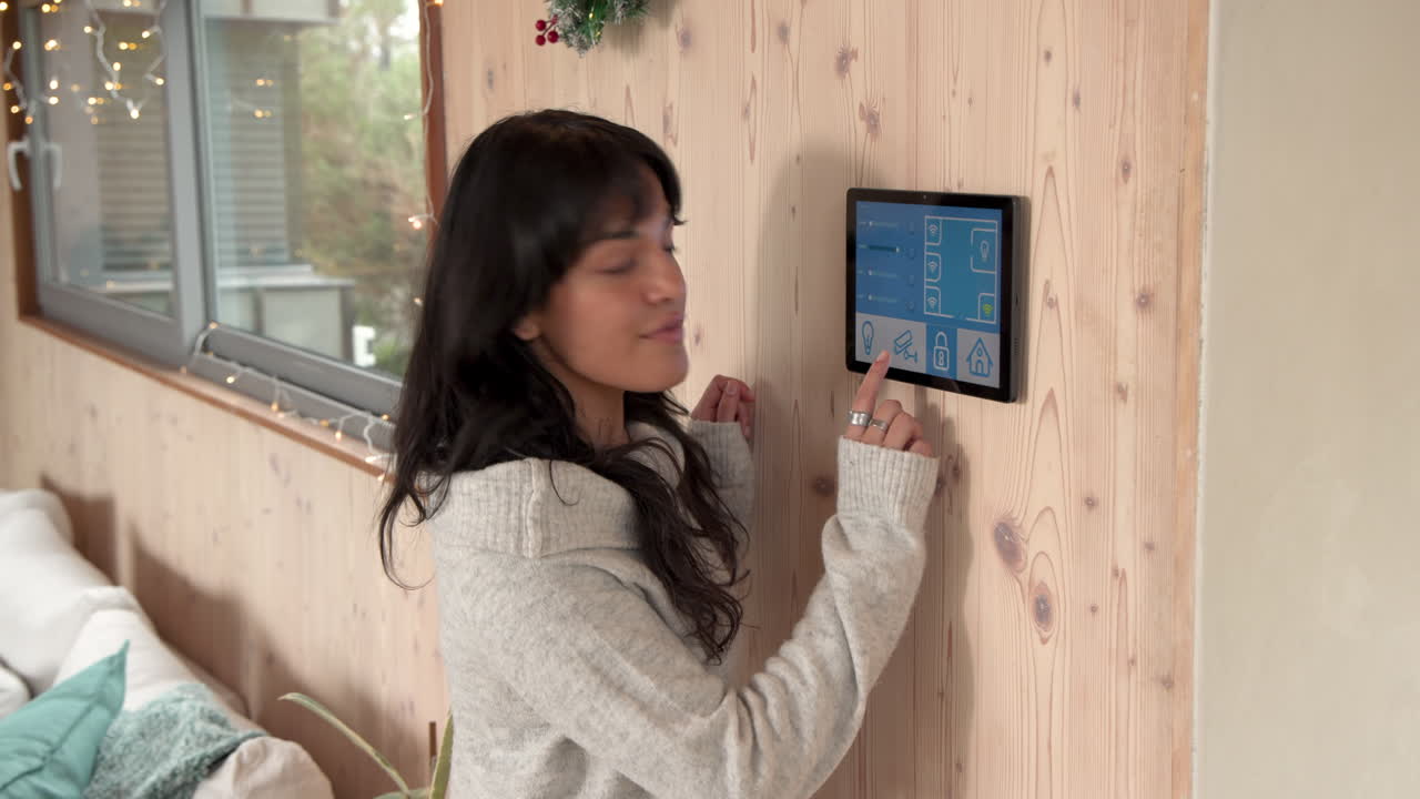 Woman adjusting smart home system on wall, smiling in cozy holiday setting