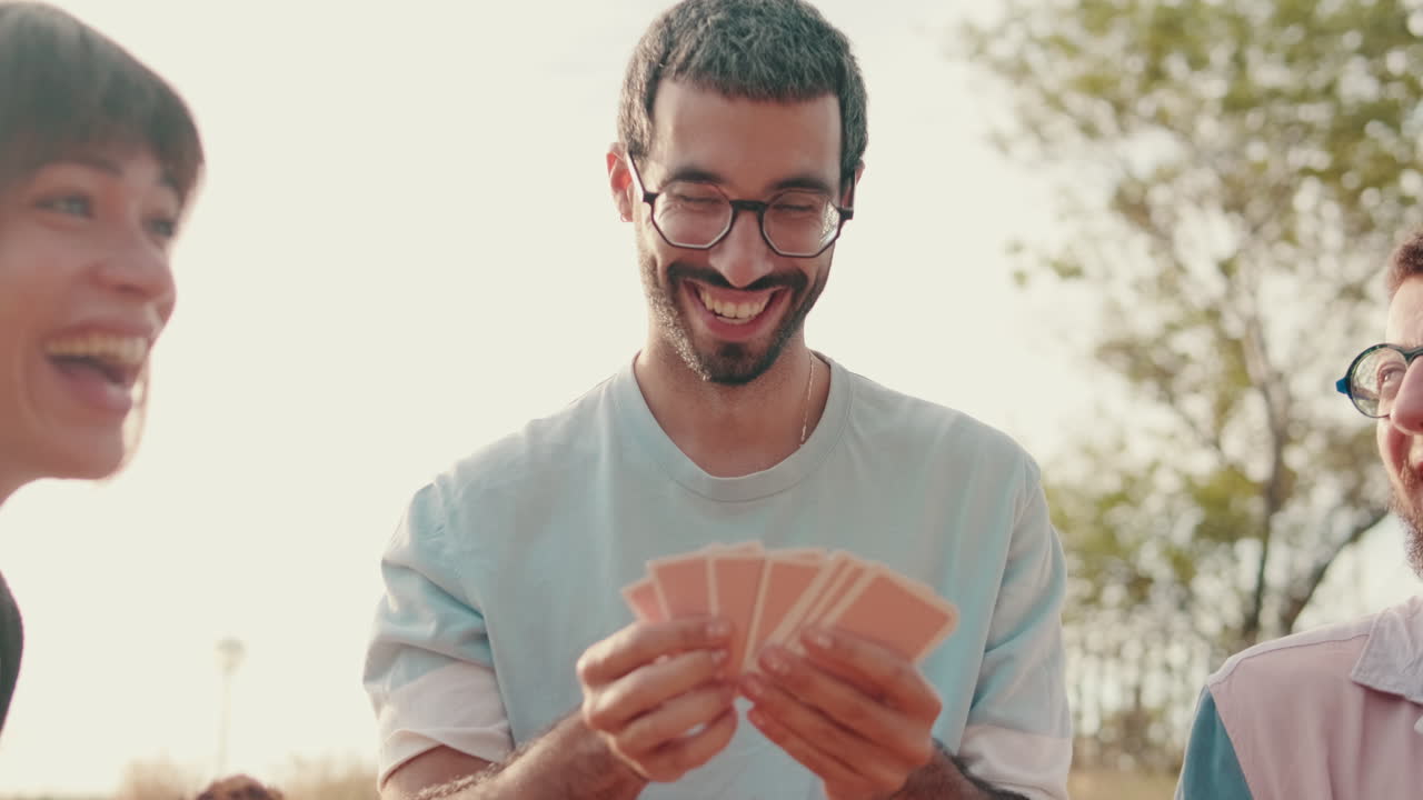 Amici che giocano a carte durante un picnic soleggiato, attenzione al giovane