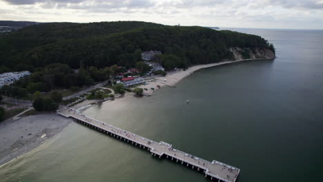 Vista-Aérea-Que-Muestra-Al-Turista-En-La-Pasarela-Del-Puerto-En-Gdynia-Orlowo-Con-Molinos-De-Maleza-En-Segundo-Plano