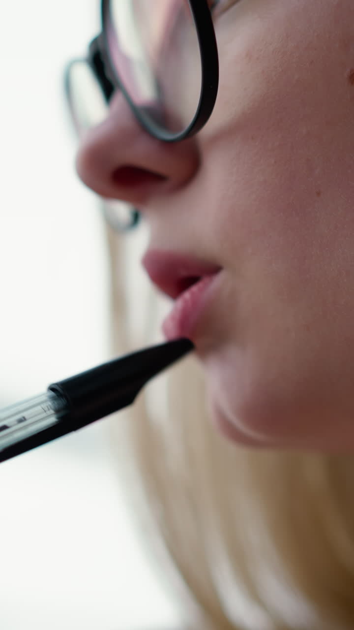 primer plano de una mujer joven girando el bolígrafo suavemente en los labios, profundamente pensativa, contemplativa, pausa intelectual, enfoque creativo, momento de reflexión, reflexión sobre ideas