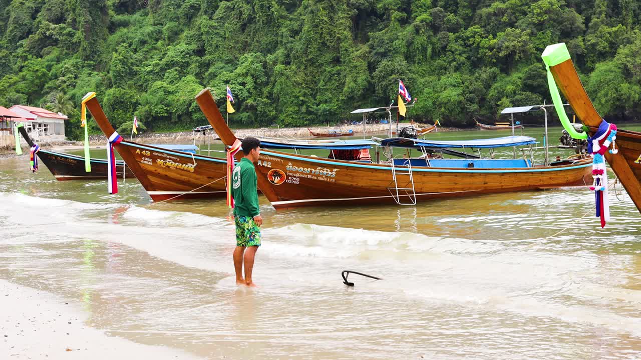 롱테일 보트 근처의 해변에 서 있는 남자