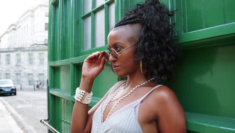 Trendy-young-black-woman-in-camisole-leaning-on-green-wall-at-the-street,-side-view,-close-up