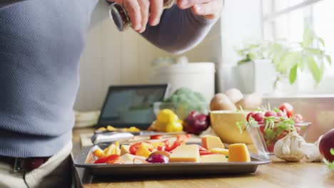 Midsection-of-caucasian-man-standing-in-kitchen,-cooking-dinner,-seasoning-food