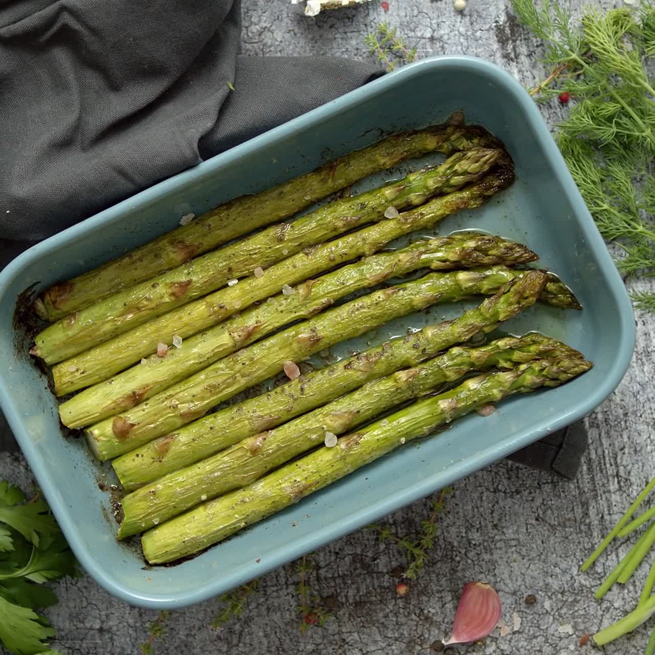 Asparagi arrosto conditi con sale, pepe e aglio, decorati con erbe fresche.