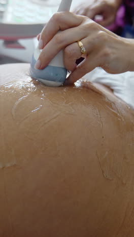 hands of future parents on the big pregnant belly. doctor moves transducer by the gelled abdomen. close up. vertical video