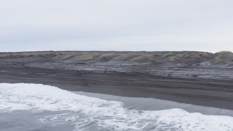 quad bike pulling a wheelie on black sand beach in iceland, aerial