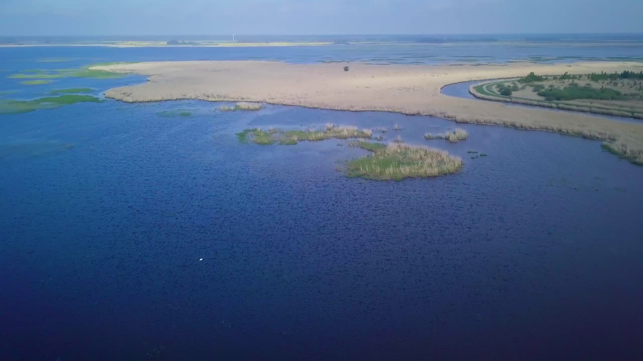 vista aérea del lago cubierto de juncos marrones y agua azul, lago liepaja, letonia, día soleado, clima tranquilo, disparo de drones de gran angular avanzando