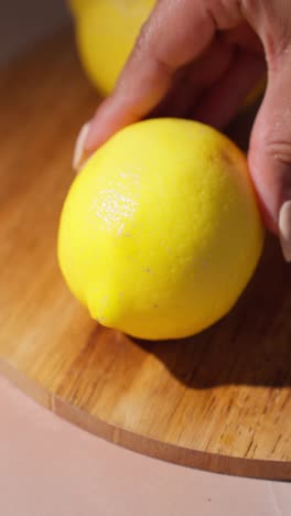 Female-cutting-into-lemon-over-wooden-cutting-board,-hard-natural-lighting