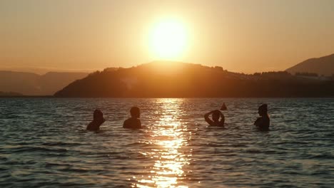 Four-people-swimming-in-winter-lake,-during-sunset