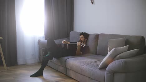un joven relajándose en el sofá y tocando la guitarra