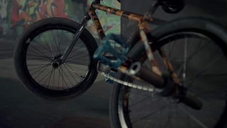 bmx bike parking against ramp at skatepark graffiti wall. bicycle wheel spinning