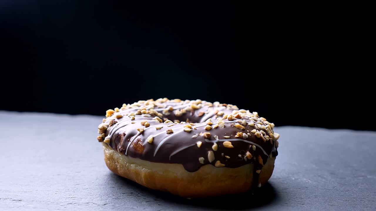 girando alrededor de un disparo de deliciosa rosquilla de chocolate esmaltado con nueces trituradas y tapa blanca girando lentamente sobre el fondo de la mesa gris.