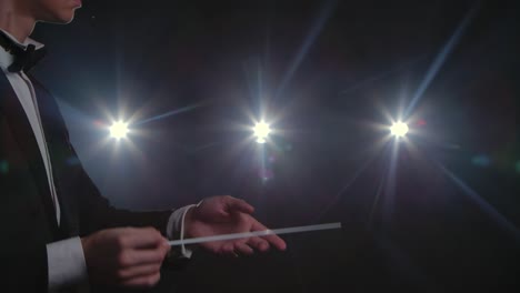 moving hands of an orchestra conductor directing musicians with movement of baton on black background with lights. conducting, directing classical musical performance with visible gestures. close up