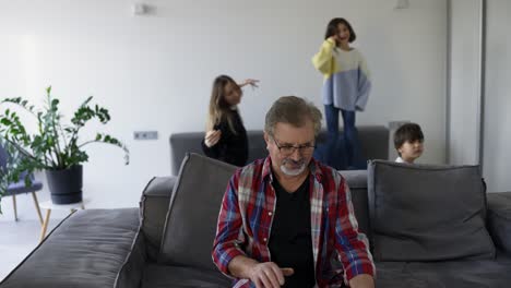 los nietos están jugando en el fondo mientras el abuelo usa la computadora portátil en casa