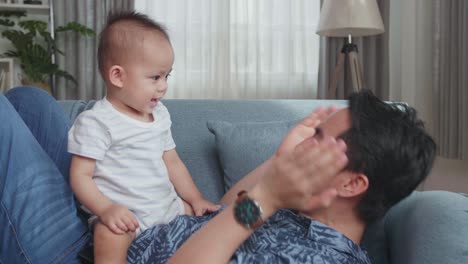 asian father and son playing on sofa in home