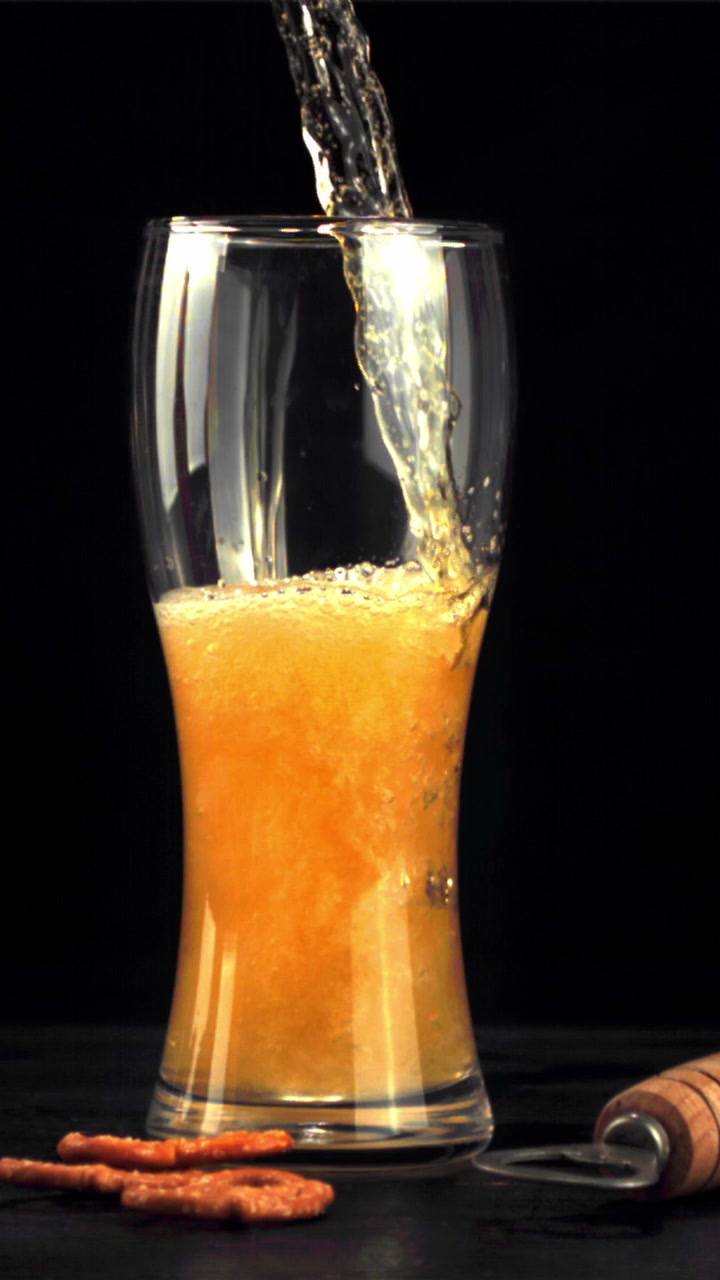 Birra dorata versata in un bicchiere con pretzel e apribottiglie