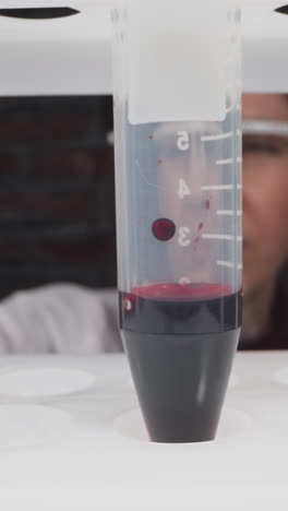 doctor turns plastic test tube with scale and blood sample in laboratory slow motion. probe lens footage of disease research macro view