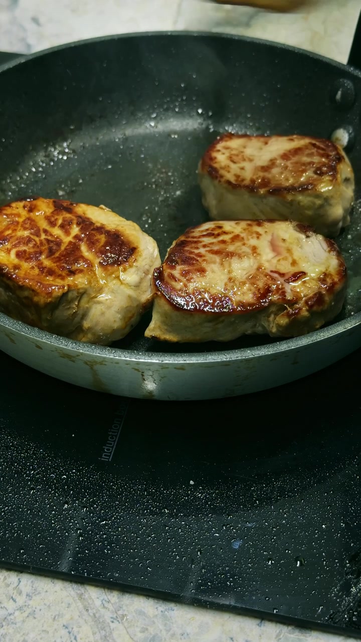 Close-up of a chef removing perfectly cooked pork tenderloin medallions from a frying pan, leaving clean copy space for recipe endings, titles, or promotional text.