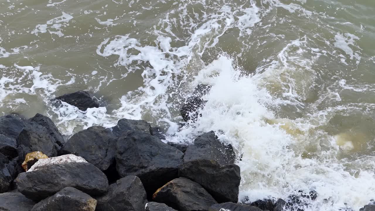 Dynamic ocean waves crash against a rocky breakwater, creating splashes and foam under natural daylight in Port Douglas, Australia