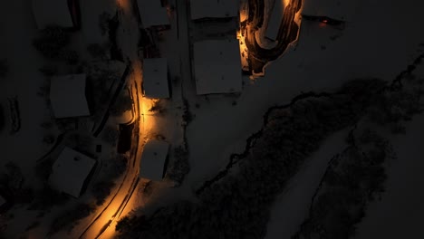 aerial top down shot of lighting curvy road on snowy mountains at night in swiss arosa city, plessur region - establishing drone shot