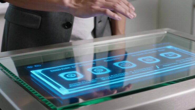 Un uomo che entra, con blazer grigio e occhiali, che si avvicina a un tavolo di vetro in laboratorio, selezionando un menu UI blu per accedere ai dati