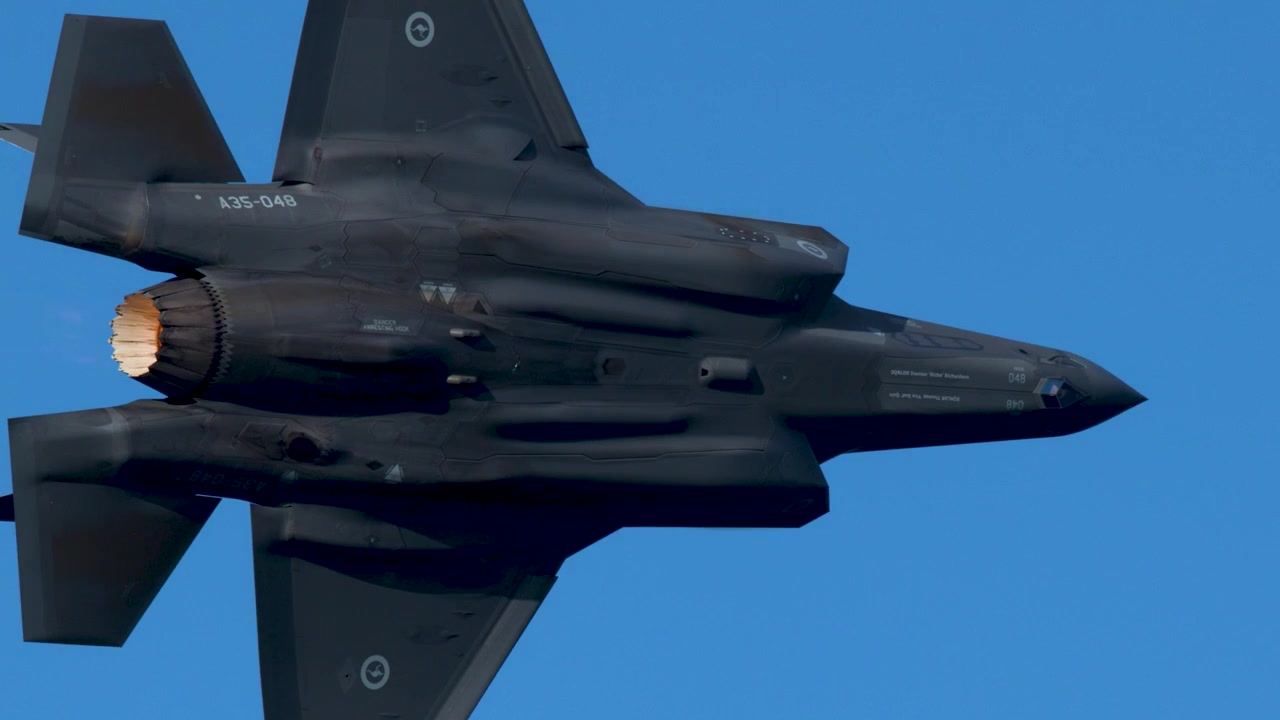Stealth fighter jet flies across clear blue sky with afterburner igniting, filmed in Australia.