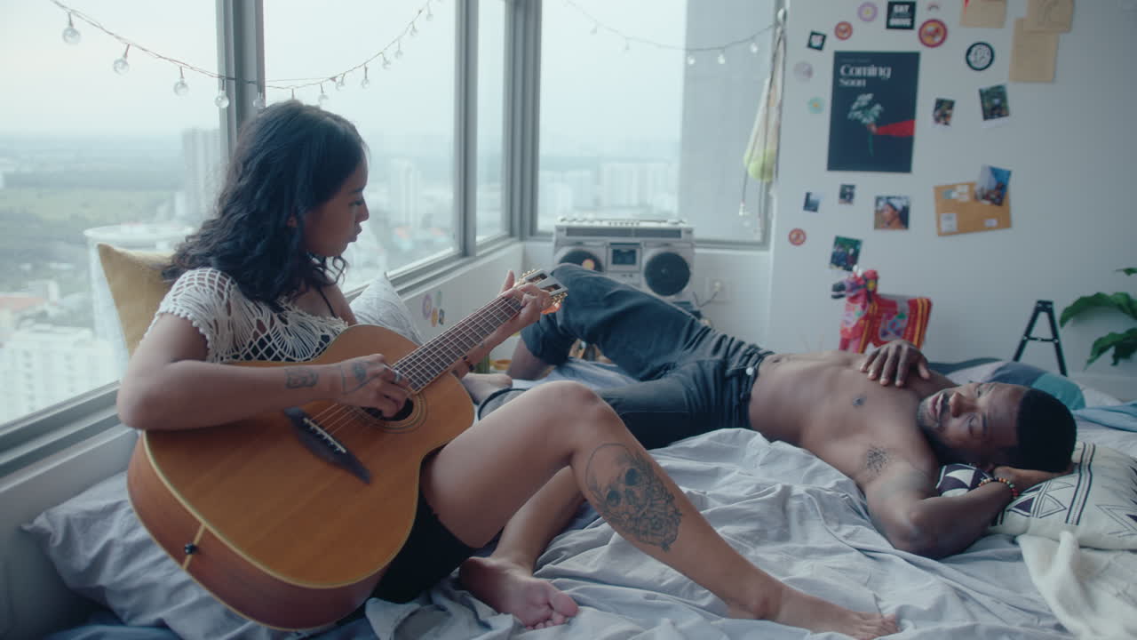 Man Chilling on Bed and Listening to Girlfriend Singing and Playing the Guitar