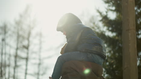 close-up of a father joyfully turning around with his son on his shoulders. both are smiling and laughing, with the sunlight casting a warm glow over them