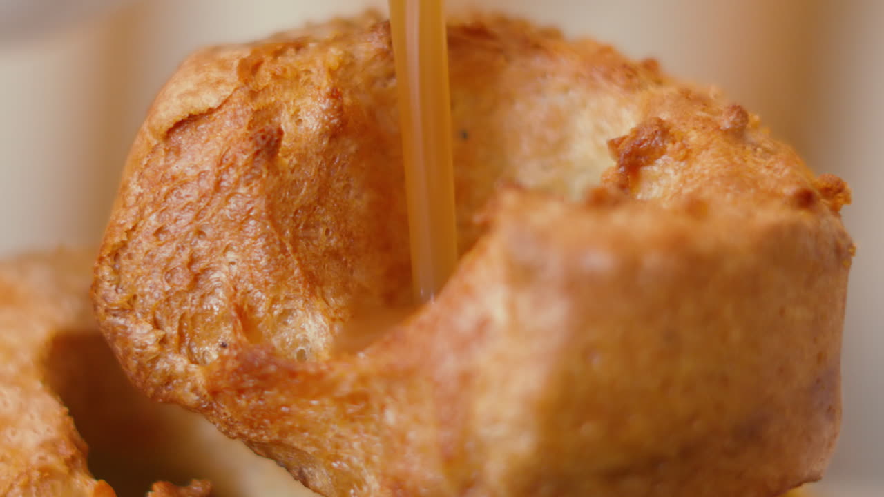 Primo piano di salsa che si versa nello Yorkshire Pudding al rallentatore con classica consistenza rustica e gonfia. Delizioso contorno per l'arrosto britannico 4K