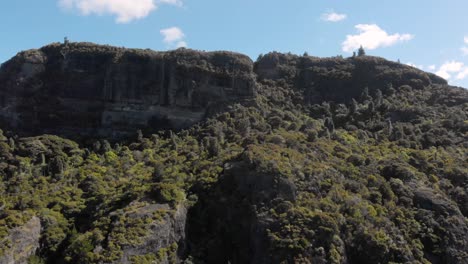 drone aéreo volando hacia arriba hacia el borde de un enorme acantilado de montaña, moviéndose sobre las rocas