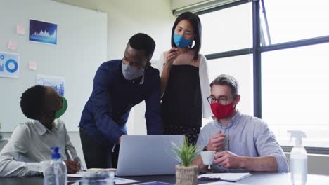 office colleagues wearing face masks using laptop together in meeting room at modern office