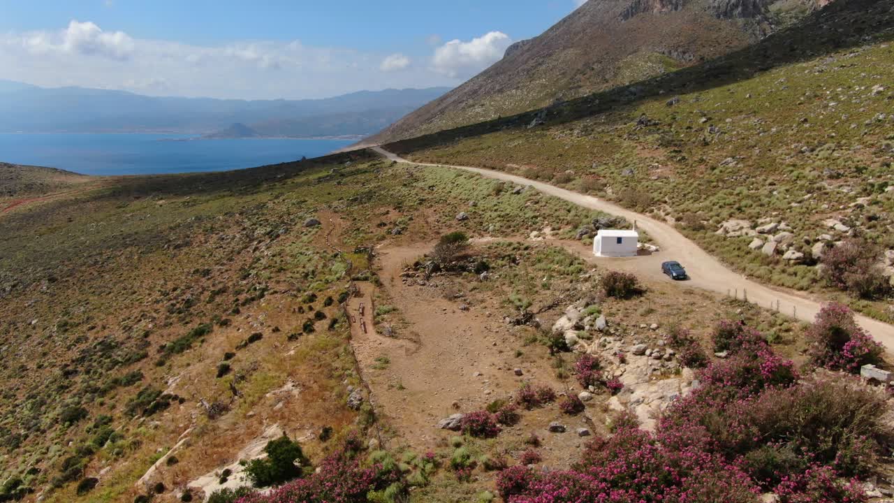 Car in Crete Greece stopped by Ekklesia Agia Irini Chapel on the road to Balos beach, Blurred plates aerial flyover shot