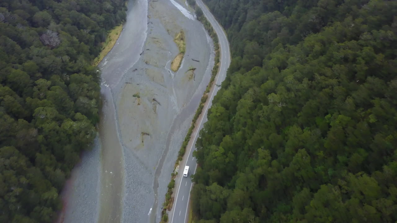 Aerial View of a Van Driving on a Scenic Road Through a Lush Forest and River Valley