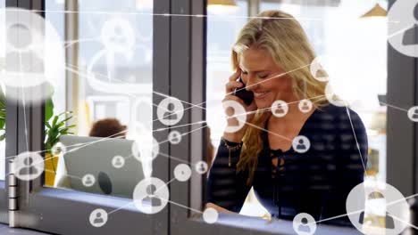 Animation-of-network-of-connections-with-icons-over-caucasian-businesswoman-talking-on-smartphone