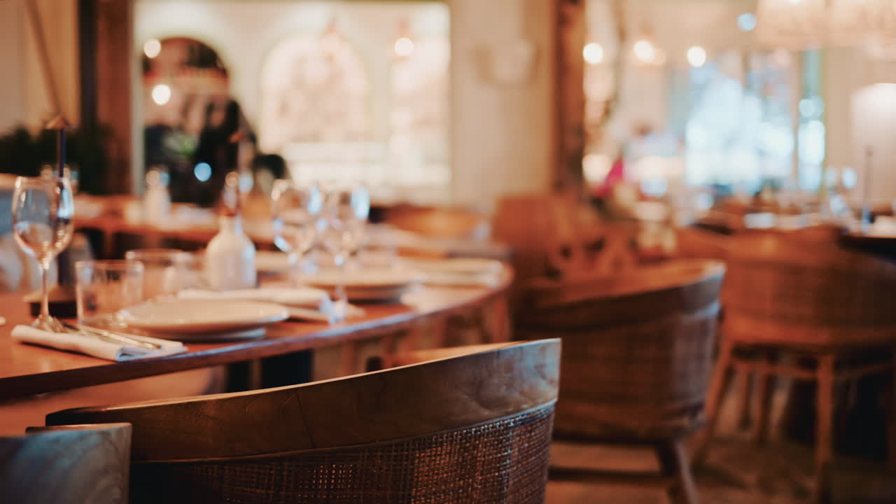 Cinematic shot of a cozy restaurant interior with warm lighting, wooden furniture, wine glasses and a refined table setup