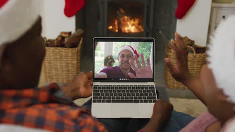 Afroamerikanisches-Paar-Mit-Weihnachtsmützen-Nutzt-Laptop-Für-Weihnachtsvideoanruf-Mit-Mann-Auf-Dem-Bildschirm