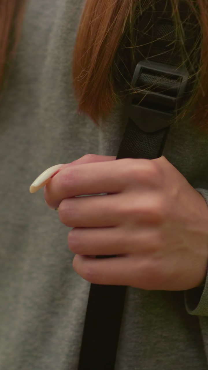 primer plano de una mujer caminando por un bosque exuberante, agarrando correas de mochila con uñas largas y cabello largo que fluye sobre los hombros, usando una sudadera gris y caminando a través de la vegetación