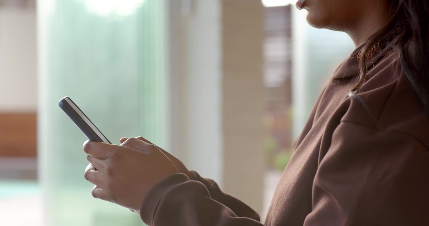 Thumbs positioned, woman is tapping and scrolling smartphone while reading aloud near window