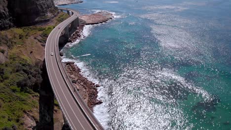 aerial view cars on sea cliff bridge, sunny day, grand pacific drive, new south wales, australia - reveal drone shot