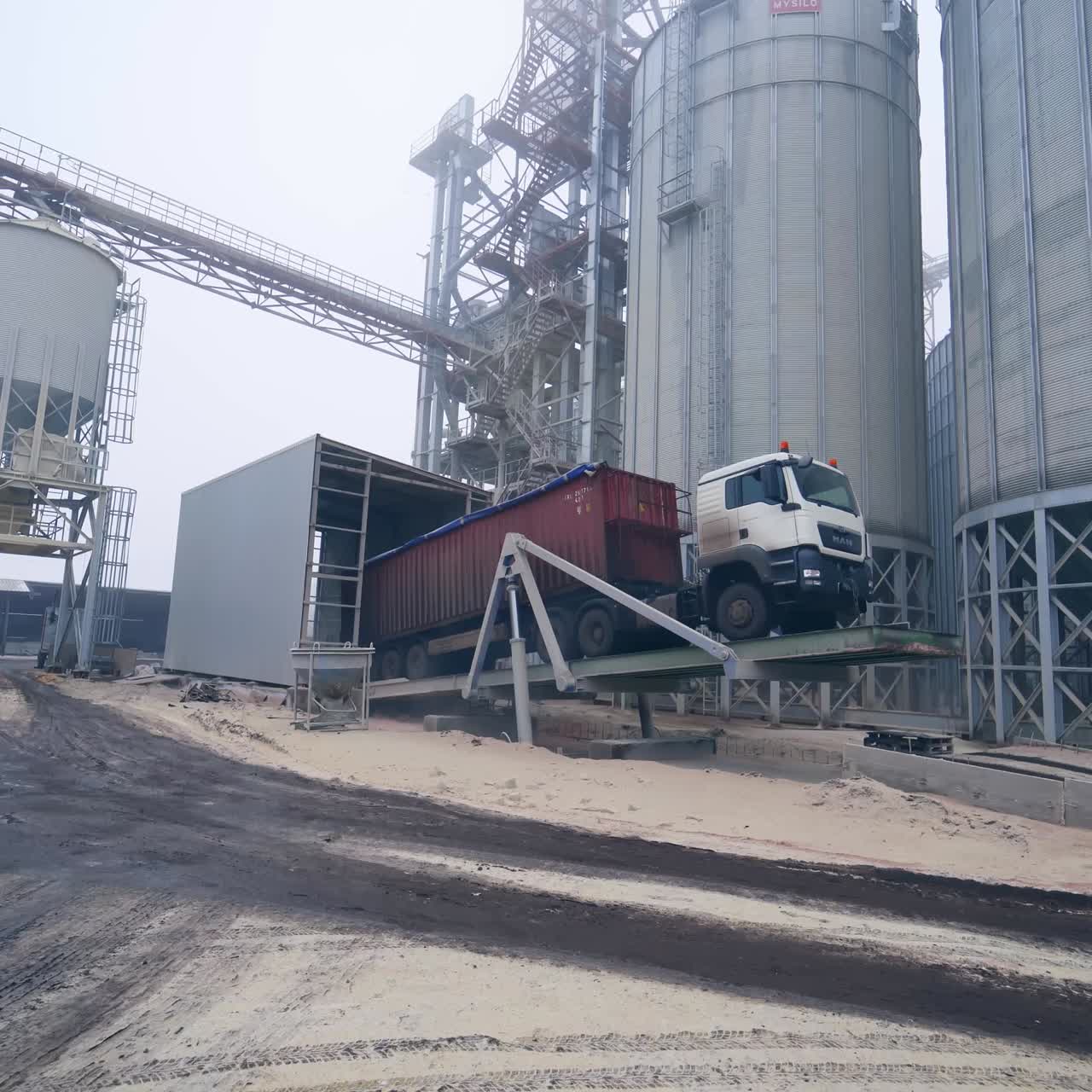 Unloading crops from a lorry to grain storage. Lorry standing on a special platform to ease the process of unloading. Loaded truck at the backdrop of elevator factory