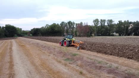 vista aérea de un tractor de arado de suelo en una granja grande en un día nublado, tiro amplio en órbita