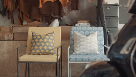 blue and yellow textile cushions and pillowcases in workshop with rawhide leather haning in the background and a portion of a vespa in the foreground