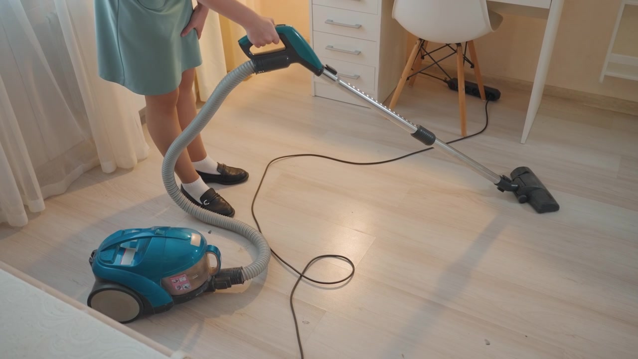 Mulher aspirando piso de madeira clara. Escritório doméstico iluminado com mesa e cadeira, aspirador cilíndrico turquesa e cabo arrastando, luz solar suave da manhã, interior minimalista e arrumado, proprietária realizando a limpeza silenciosamente.