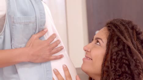 mujer sonriente besando el vientre de su novia embarazada