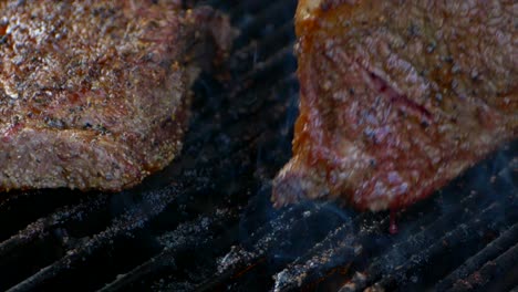 a fork turns a nearly cooked juicy rib eye steak on a grill as blood drips from it and flames shoot up in slow motion